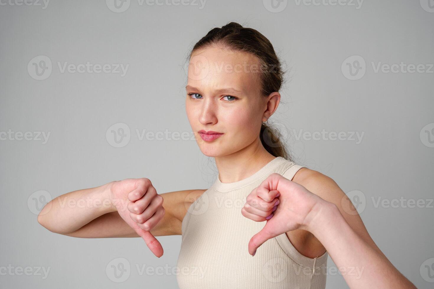 Young Woman Giving Thumbs Down Gesture Against a Neutral Background. photo