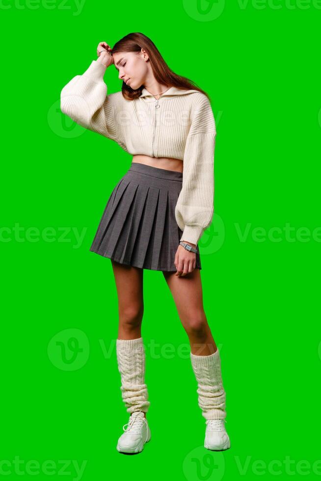 Young Woman in a White Sweater and Grey Skirt Standing Against a Green Background photo