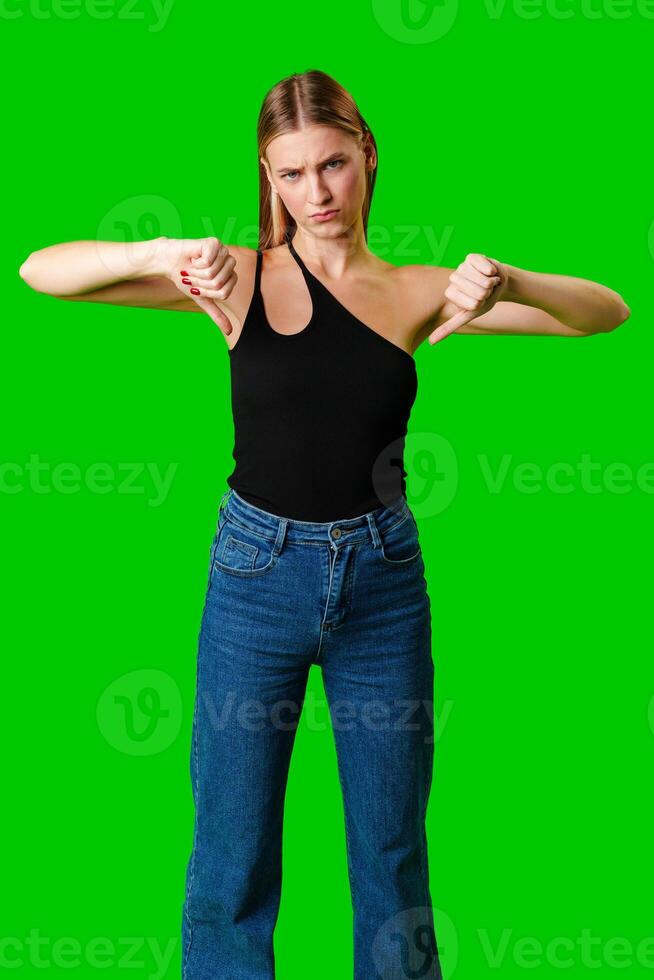 Young Woman Expressing Disapproval With a Thumbs Down Gesture Against a Green Background photo