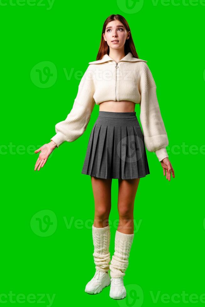 A woman is standing on a green screen backdrop, wearing a skirt and sweater. She appears poised and looking directly at the camera. photo