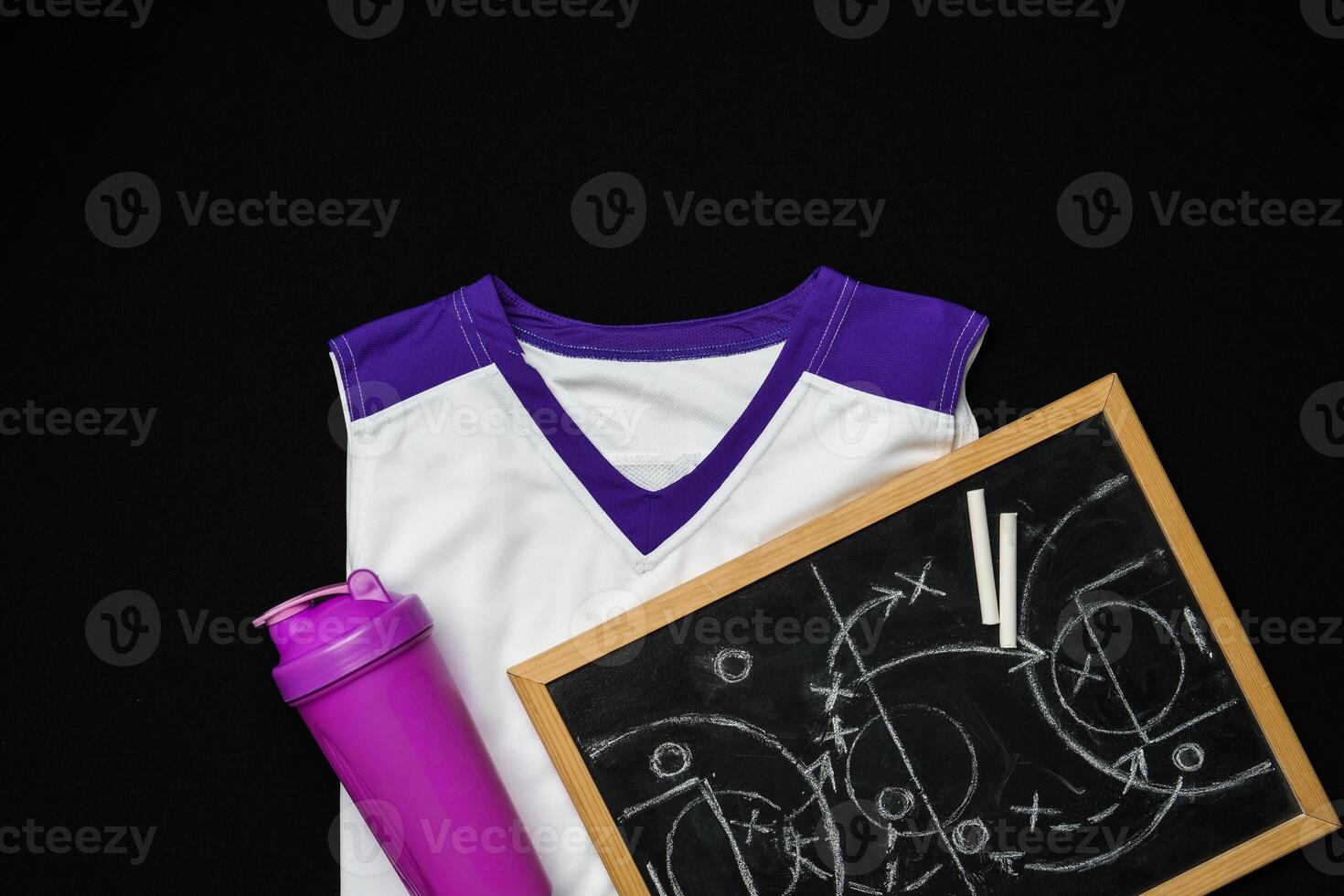 White and Purple Sports Uniform and Water Bottle Next to a Chalkboard on Black Background photo