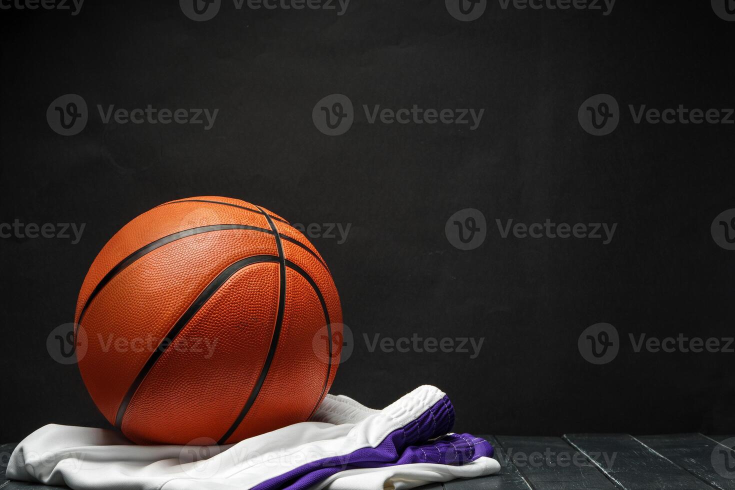 Vibrant Orange Basketball Resting on a Dark Wooden Floor With White and Purple uniform photo