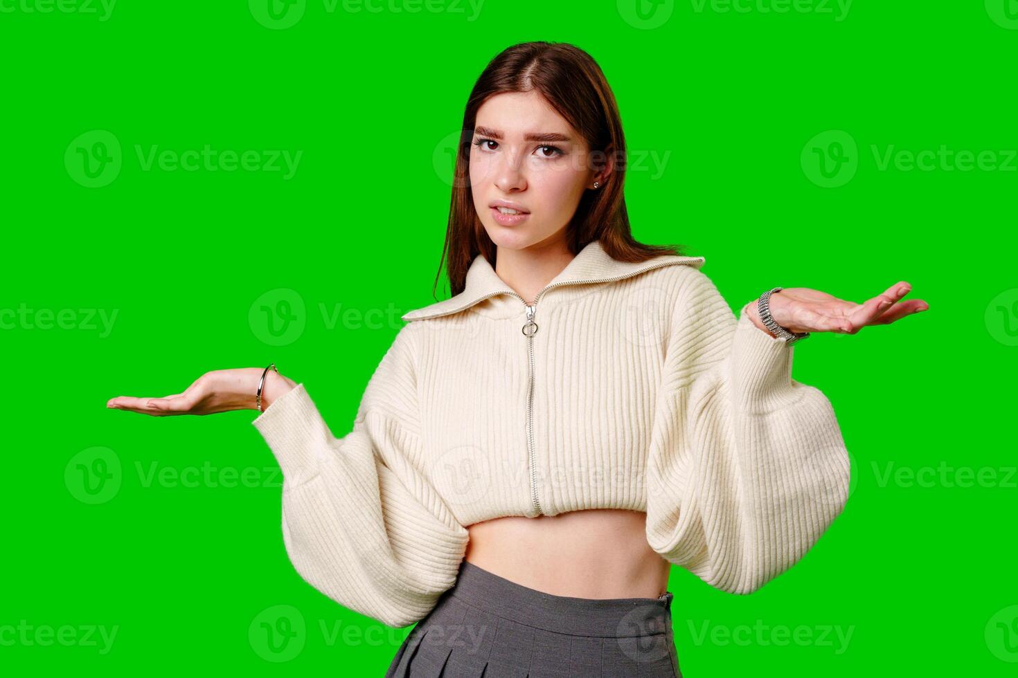 A young woman stands against a vibrant green backdrop, her expression one of uncertainty or confusion. photo