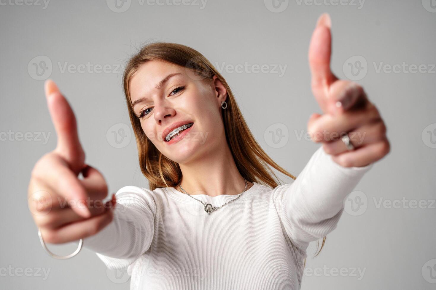 Smiling Young Woman With Braces Pointing Towards Camera in Studio photo