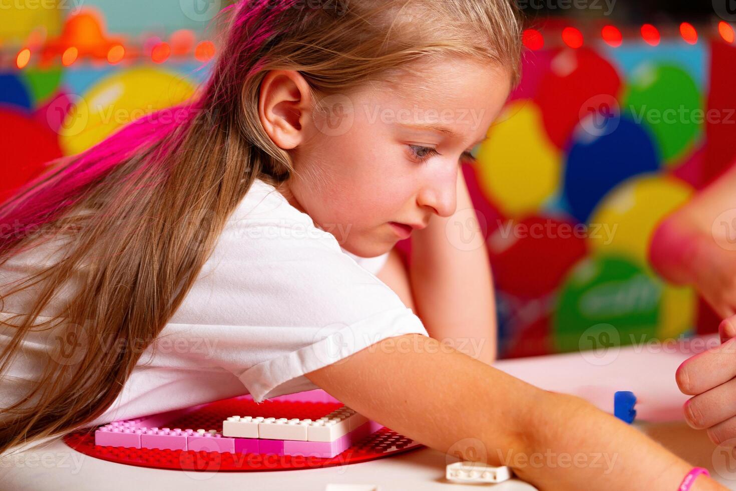 Curly-Haired Toddler Girl Concentrating on Building With Colorful Blocks Indoors photo