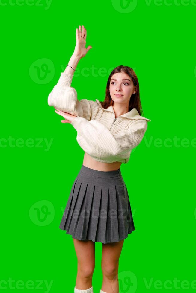 A woman dressed in a skirt and sweater is standing and waving her hand in the air, possibly in a greeting or to get someones attention. photo