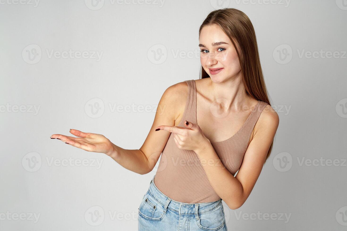 Young Woman in Tank Top Pointing at Something on gray background photo