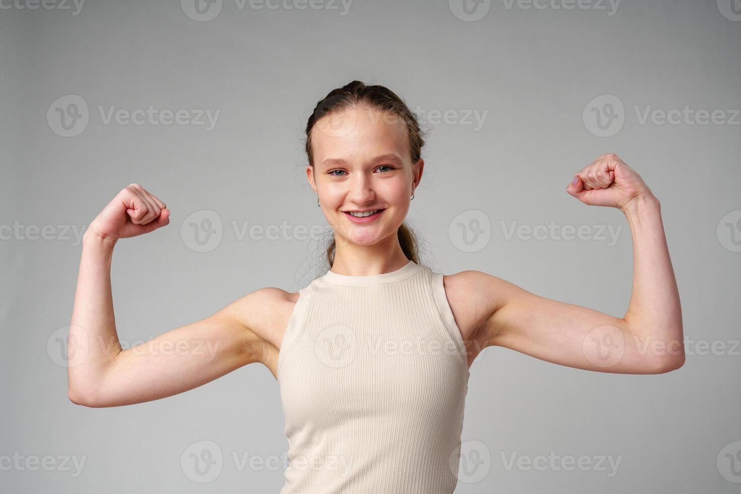 Young Woman Flexing Muscles in Beige Tank Top on gray background photo