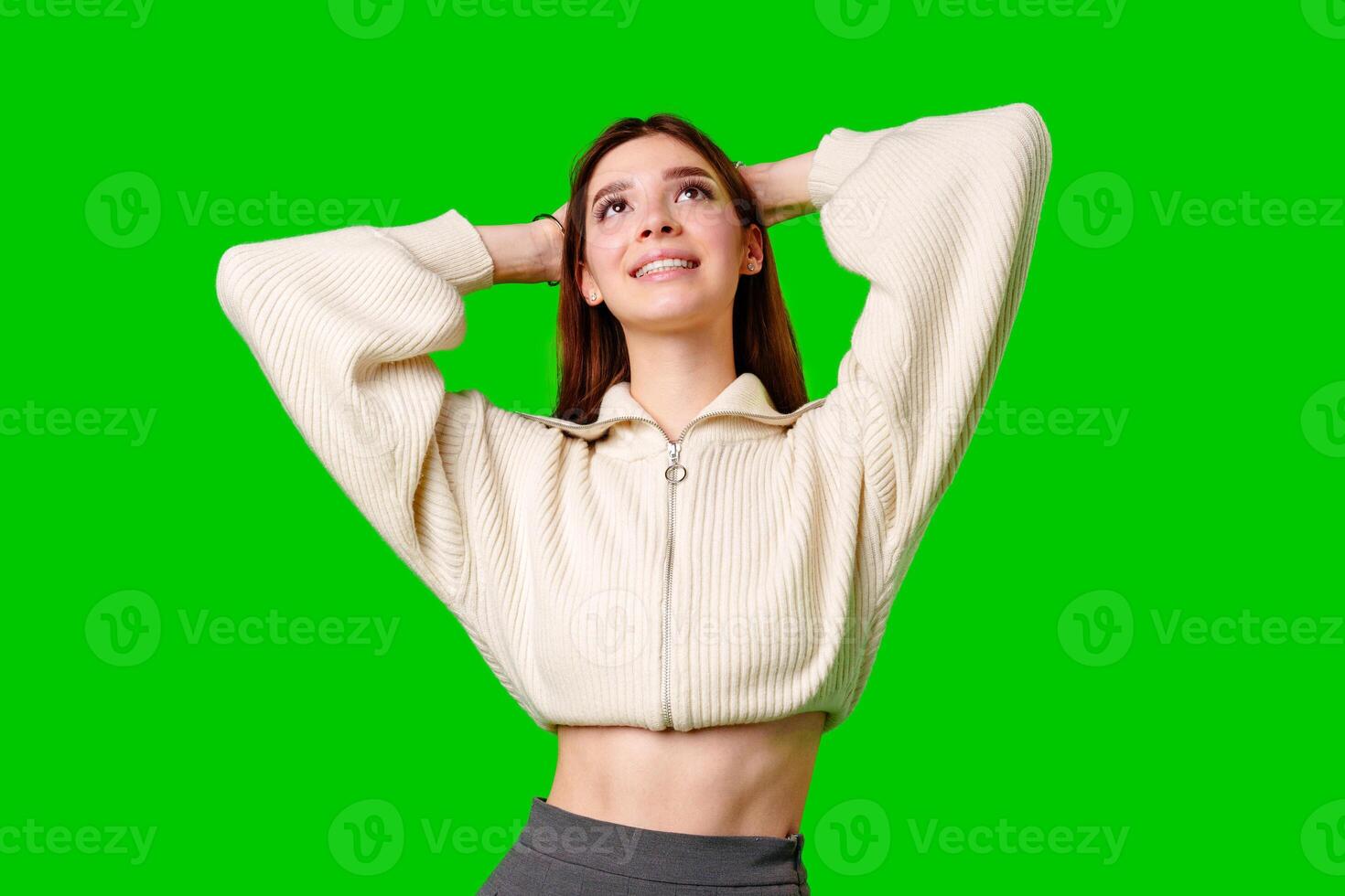 Young Woman Smiling and Looking Upward While Holding Her Hair on a Green Background photo