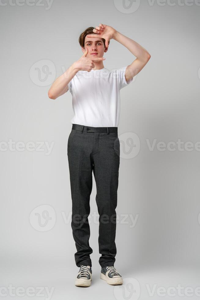 Young Man Making Frame With Hands Focusing On an Imaginary Object Against a Plain Background photo