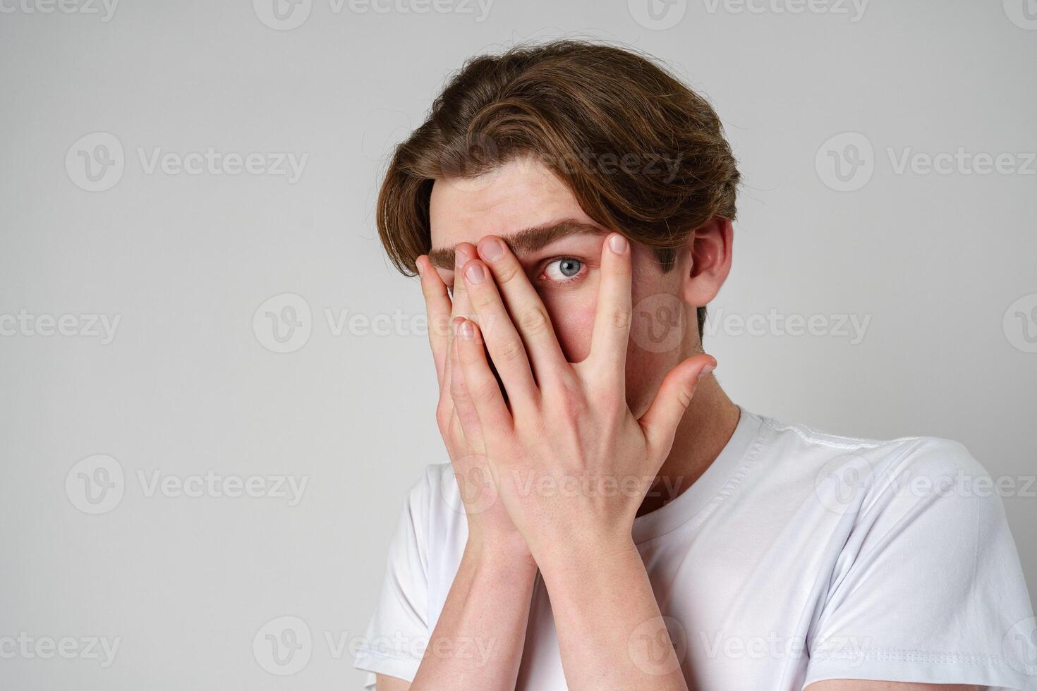 Young Man Covering His Face With His Hands Against a Neutral Background photo