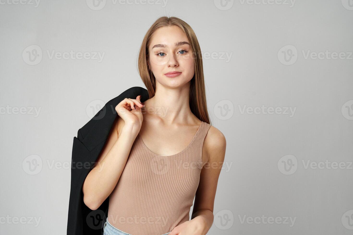 Young Woman in Casual Blazer and Jeans Smiling Against a Grey Background photo