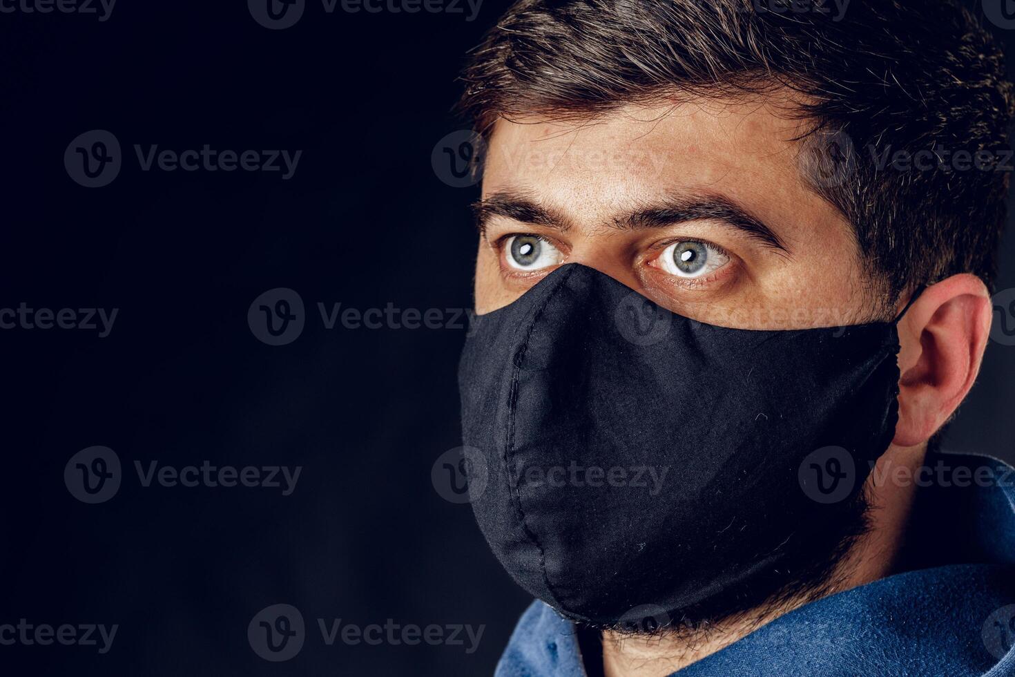 Portrait of handsome man wearing medical black mask during virus epidemic lockdown posing on dark wall. photo