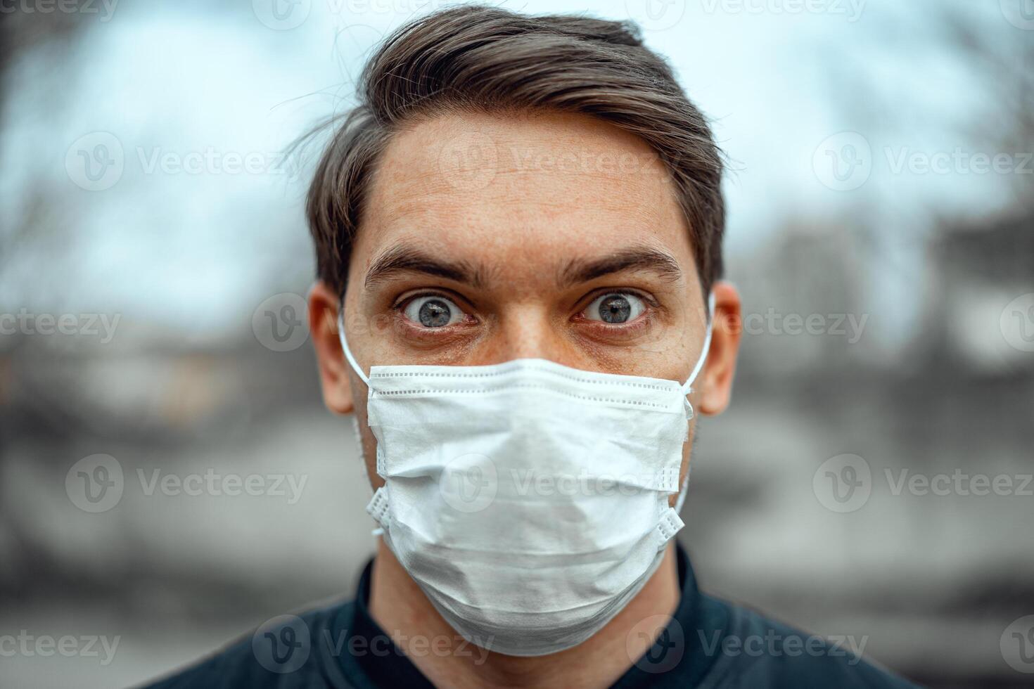Portrait man in medical mask. Young man stands on light background and looking at camera. COVID-19 Pandemic Coronavirus. photo