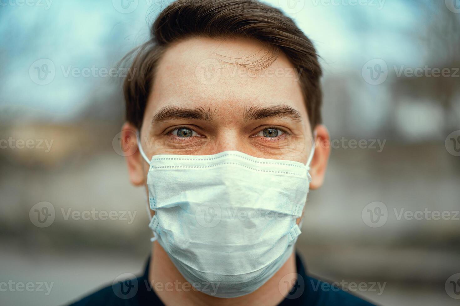 Portrait man in medical mask. Young man stands on light background and looking at camera. COVID-19 Pandemic Coronavirus. photo