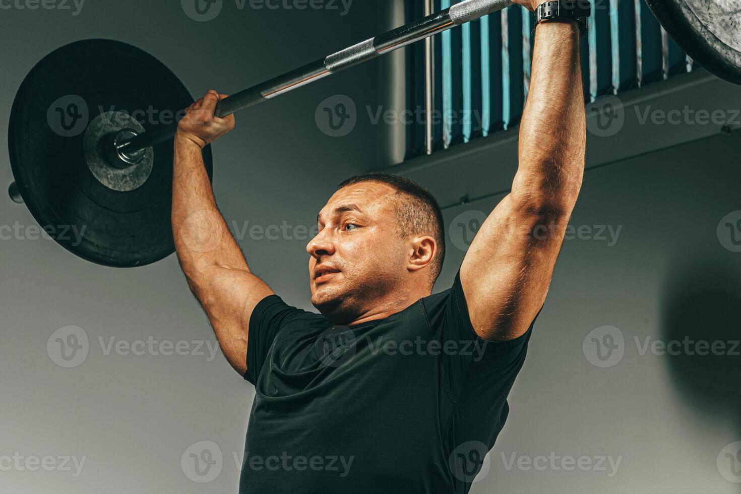 Muscular man in black sportswear lifting barbell in a gym photo