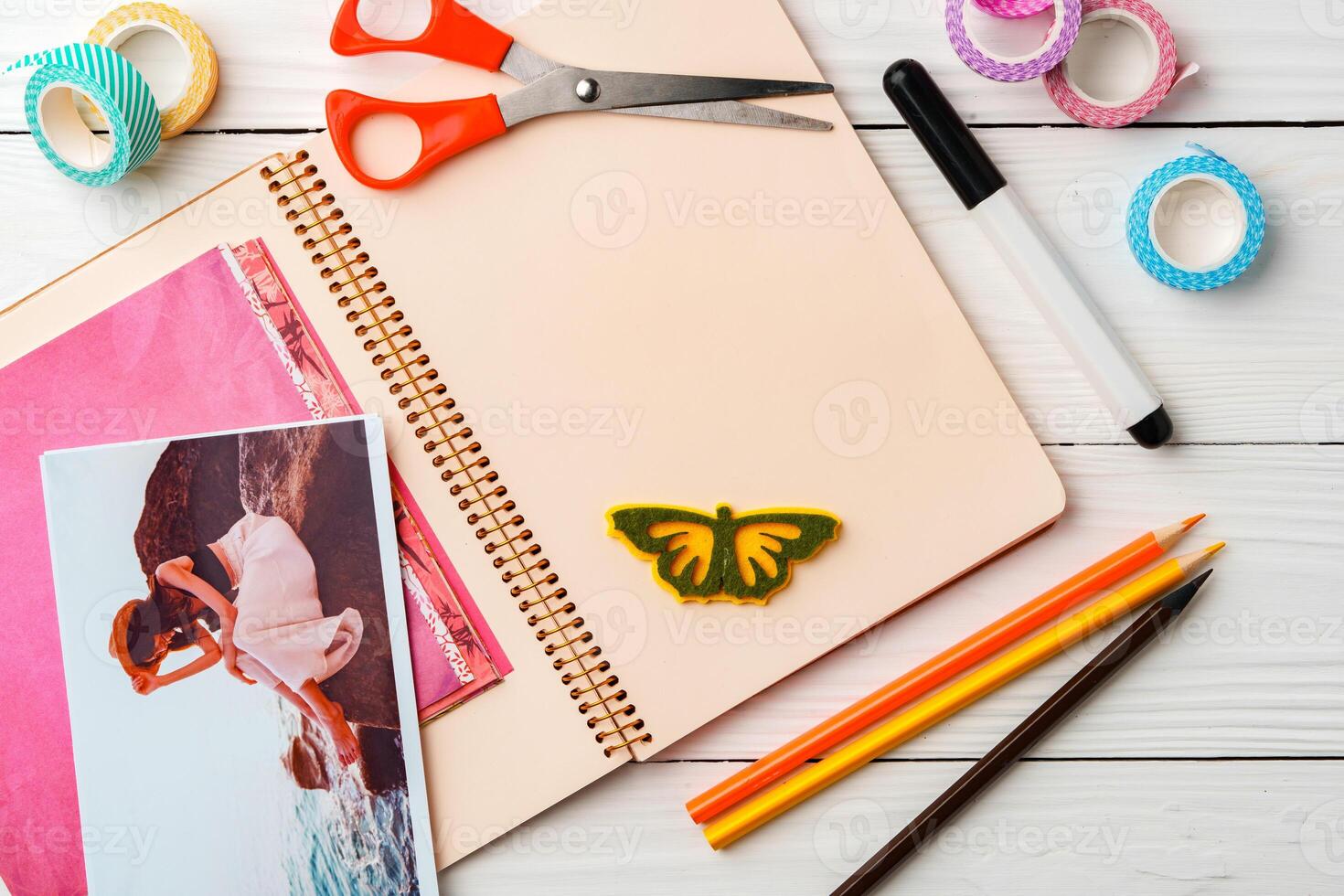 Colorful stationery arrangement with a butterfly sticker on a blank notebook at a wooden table in natural light photo