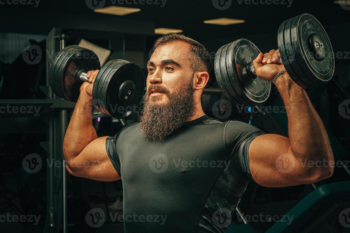 Muscular young man lifting weights in a dark gym photo