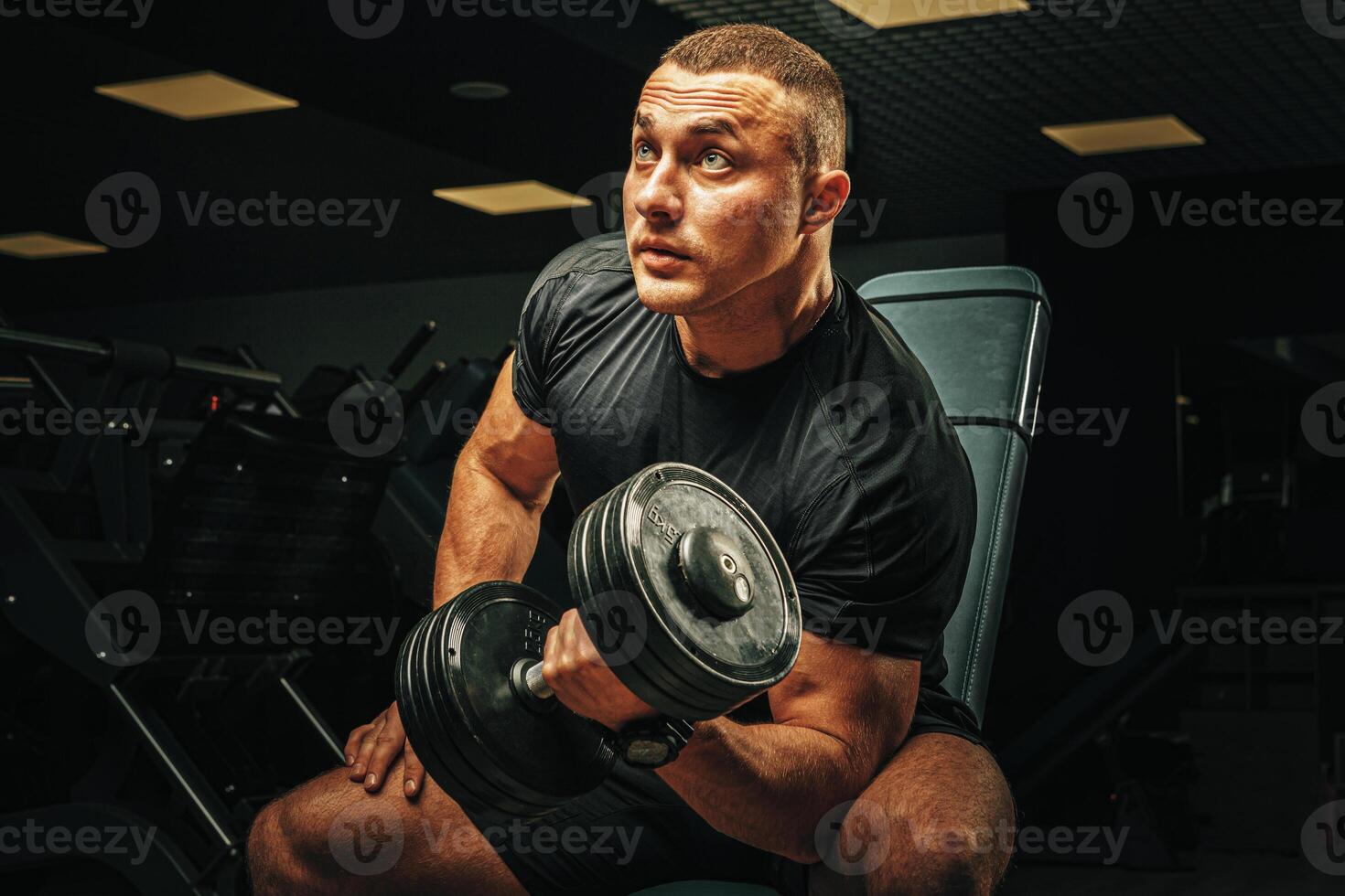 Muscular young man lifting weights in a dark gym photo