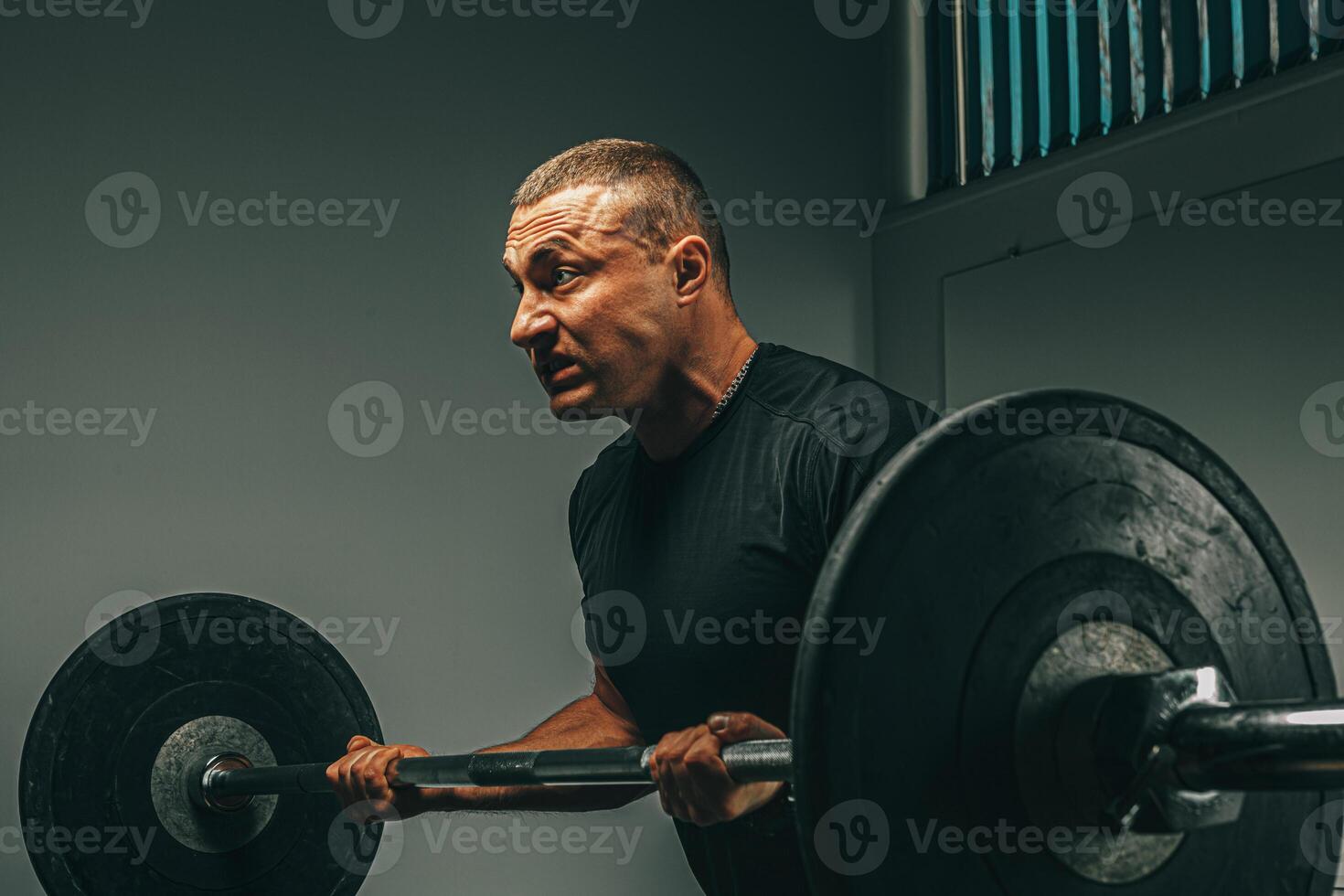 Muscular man in black sportswear lifting barbell in a gym photo