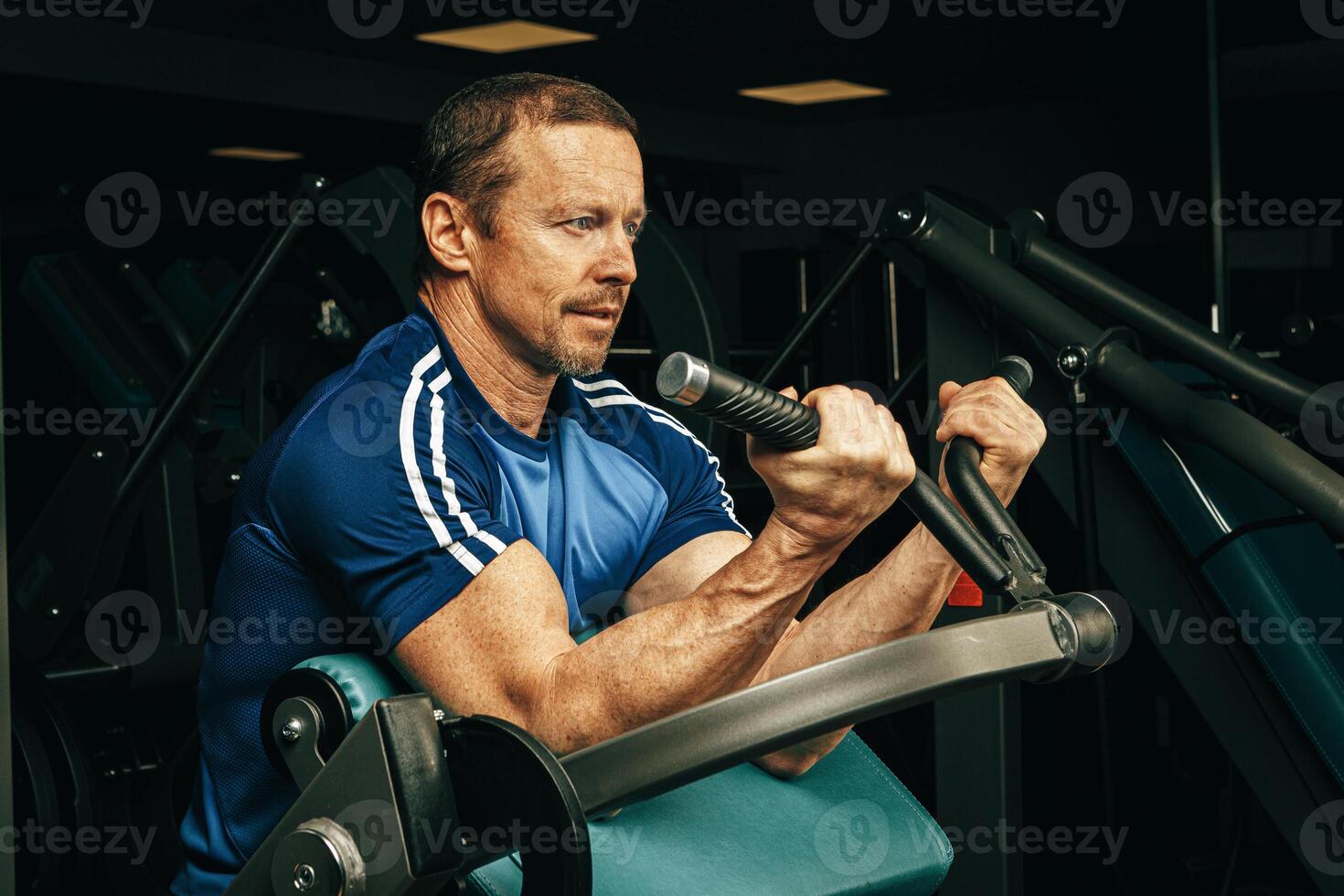 Senior man doing exercises for arms in a training machine in gym photo