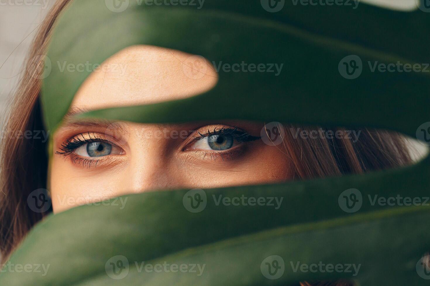 Attractive young woman hiding behind monstera leaf photo