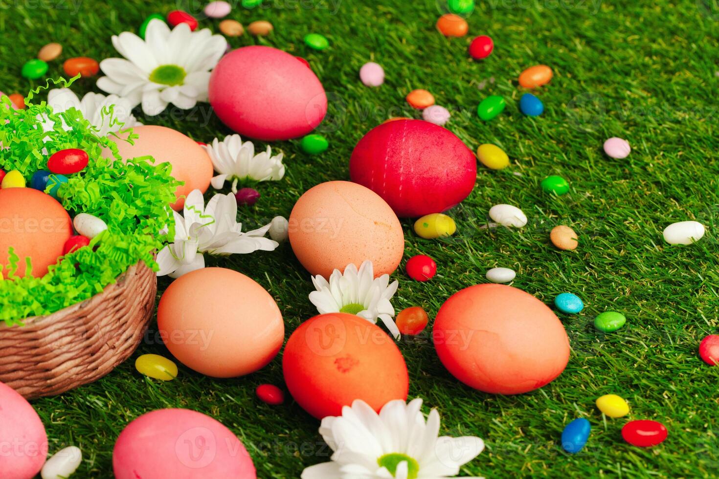 Close up photo of colored Easter eggs and candies on grass