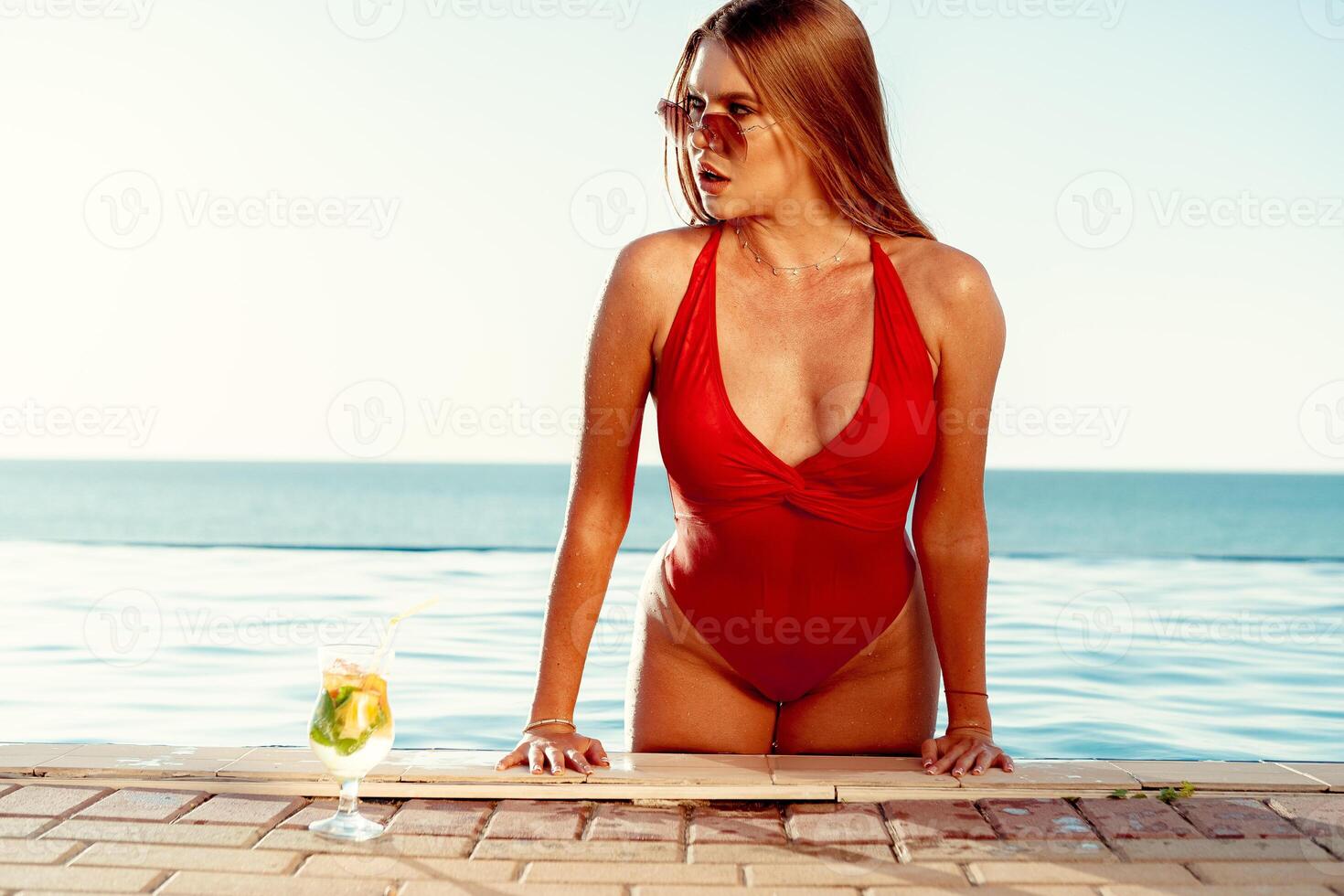 Tanned woman in red bikini in a pool with cocktail photo
