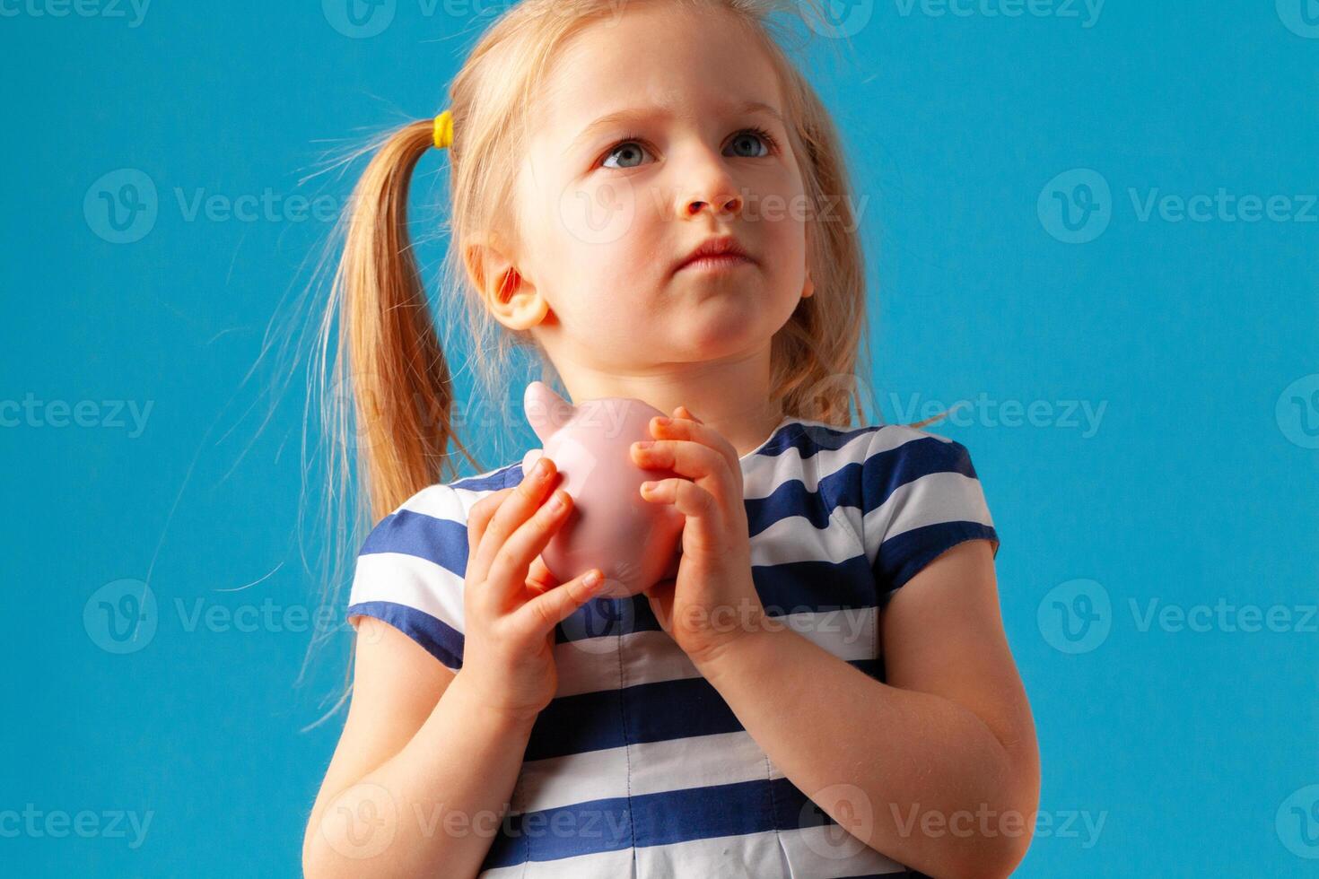 Little girl with piggy bank moneybox against blue background photo