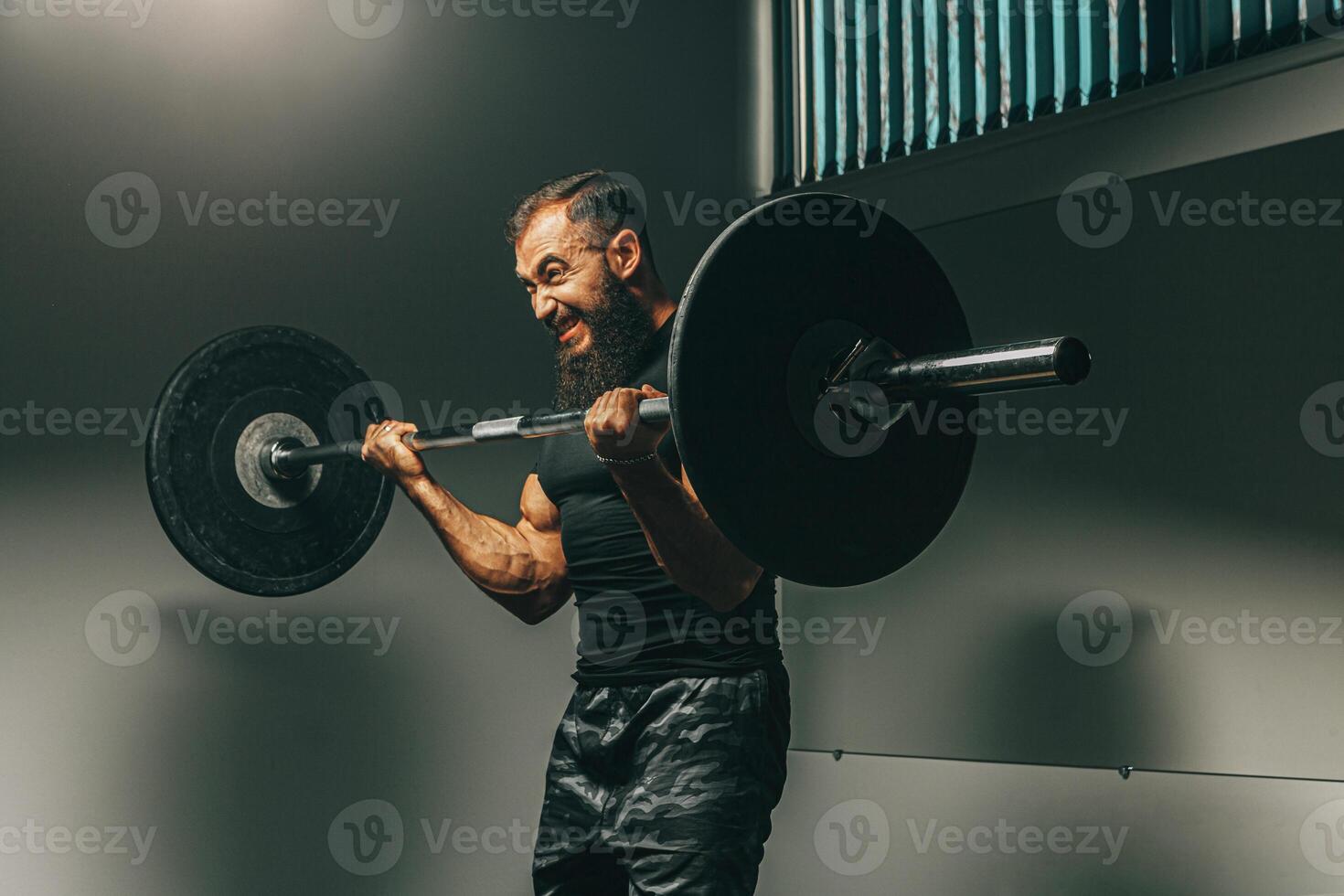 Muscular man in black sportswear lifting barbell in a gym photo