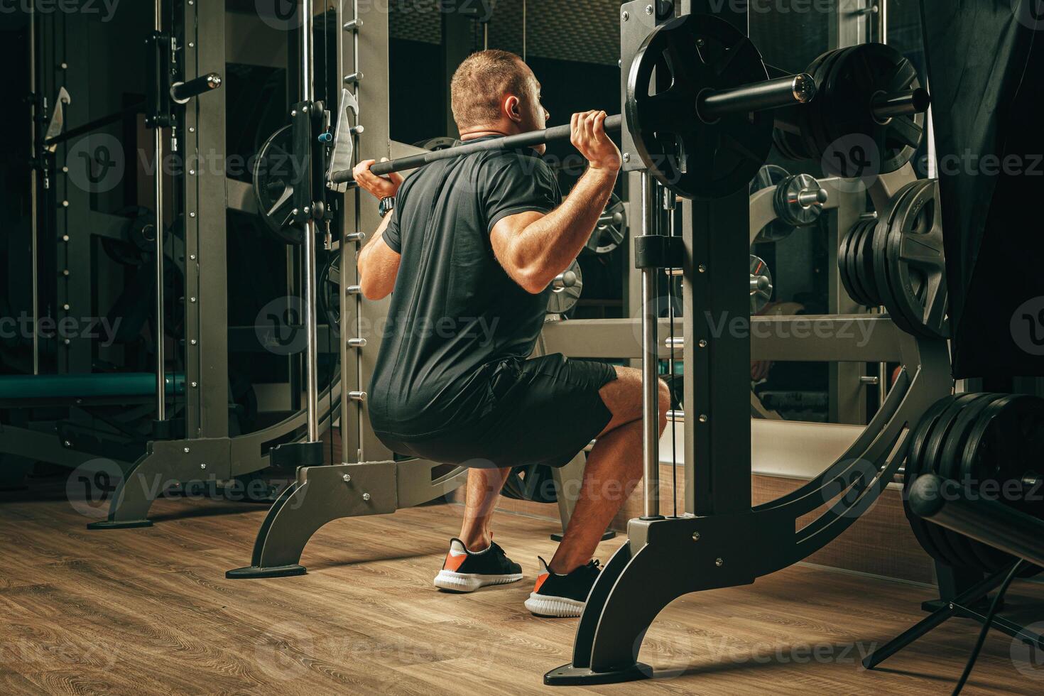 Fit man doing squats in a training machine photo