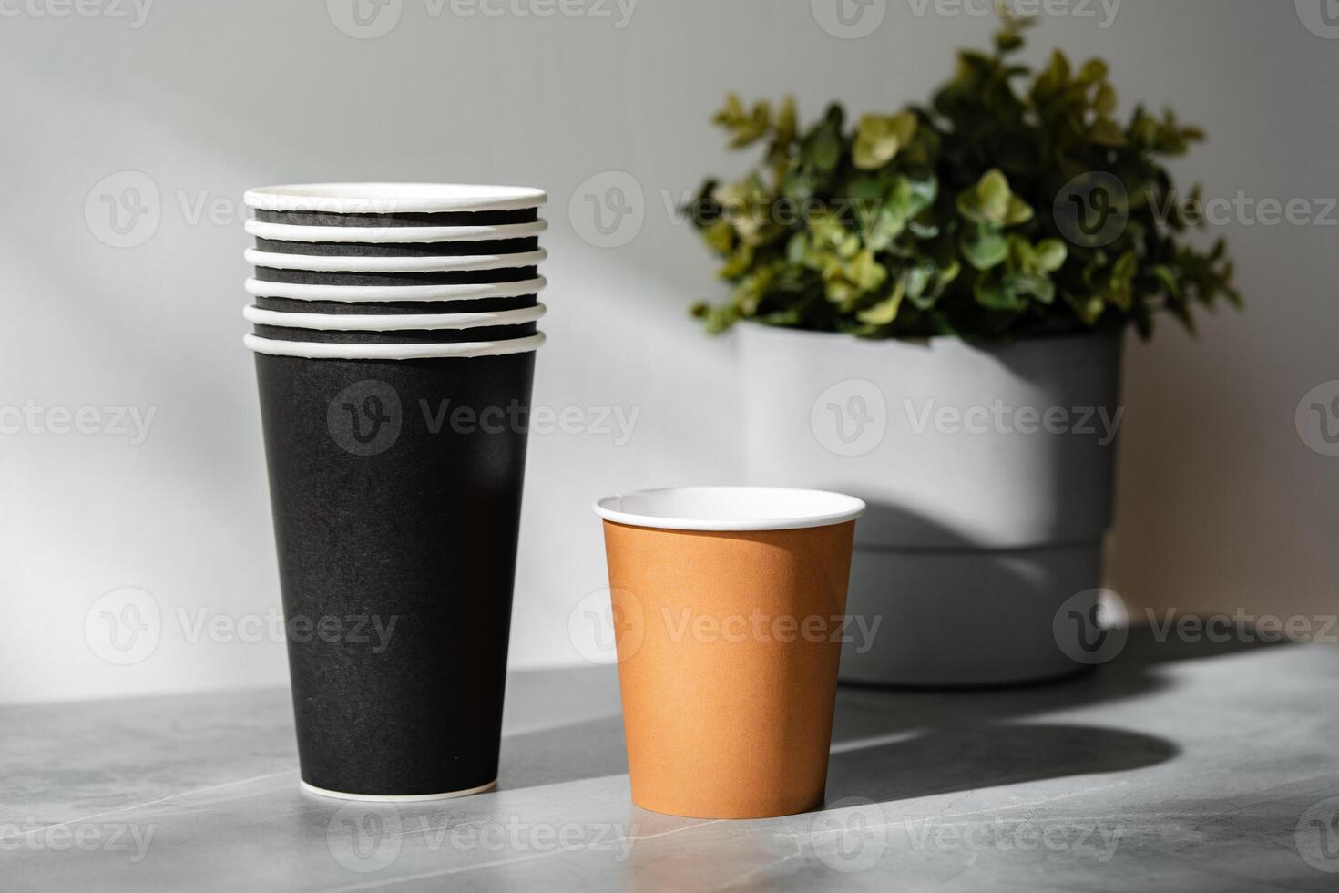 Stack of disposable cups beside a potted plant on a marble surface in natural light photo