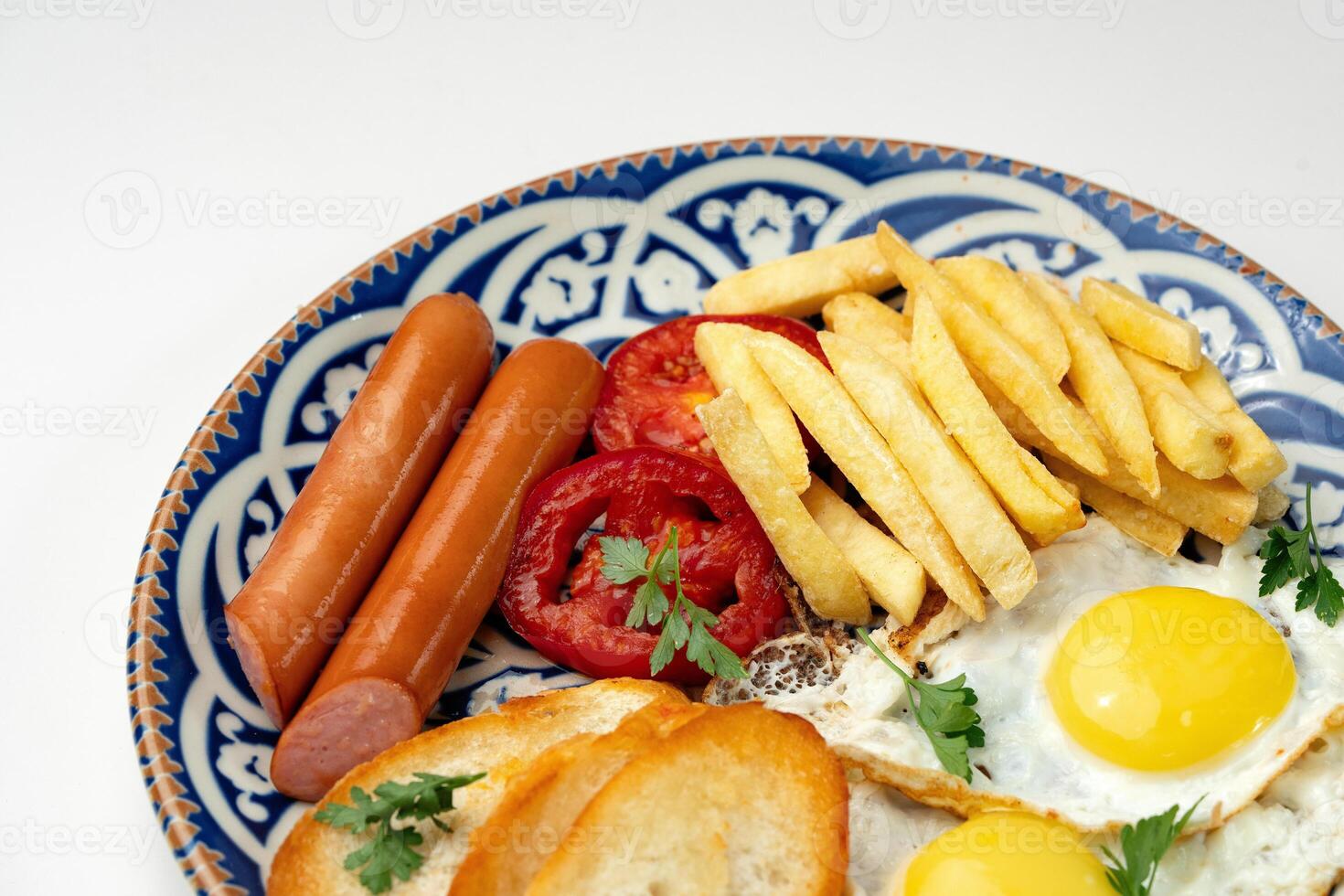 Breakfast plate with fried eggs, sausage, tomatoes, and fries served on a decorative blue plate photo