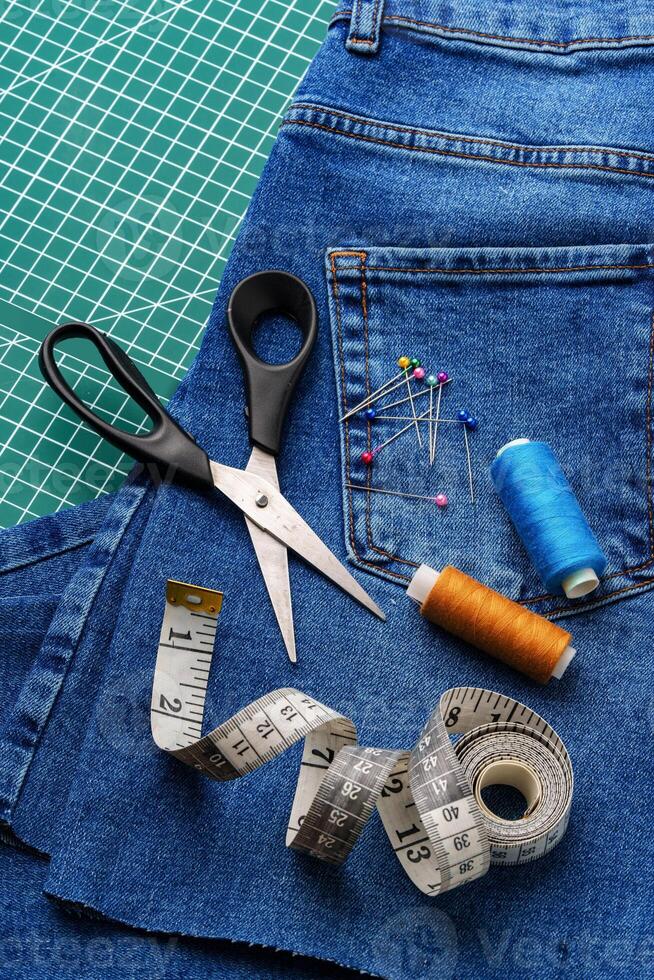 Sewing tools on a cutting mat with denim and thread spools in a craft workspace photo