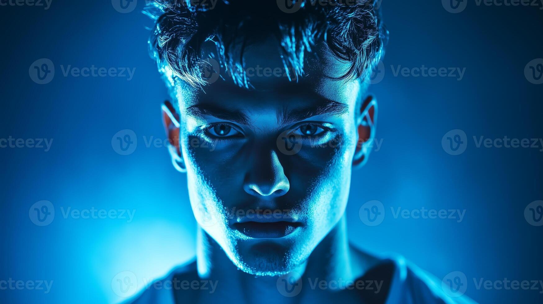 A young man with striking features poses against an intense blue background capturing an intriguing, moody atmosphere in a studio setting photo