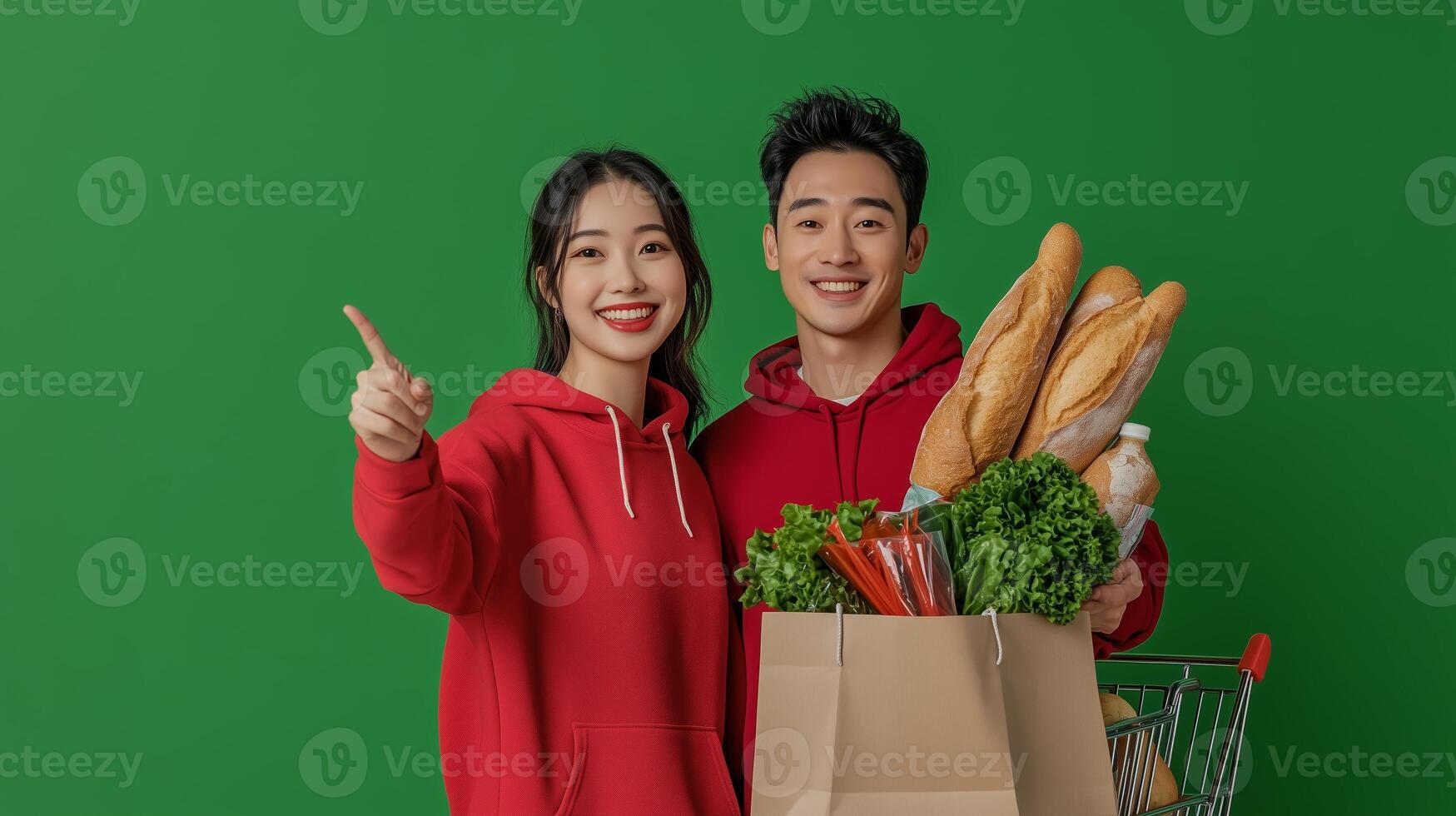 Cheerful young couple with groceries in a shopping cart on a green background enjoying their time together photo