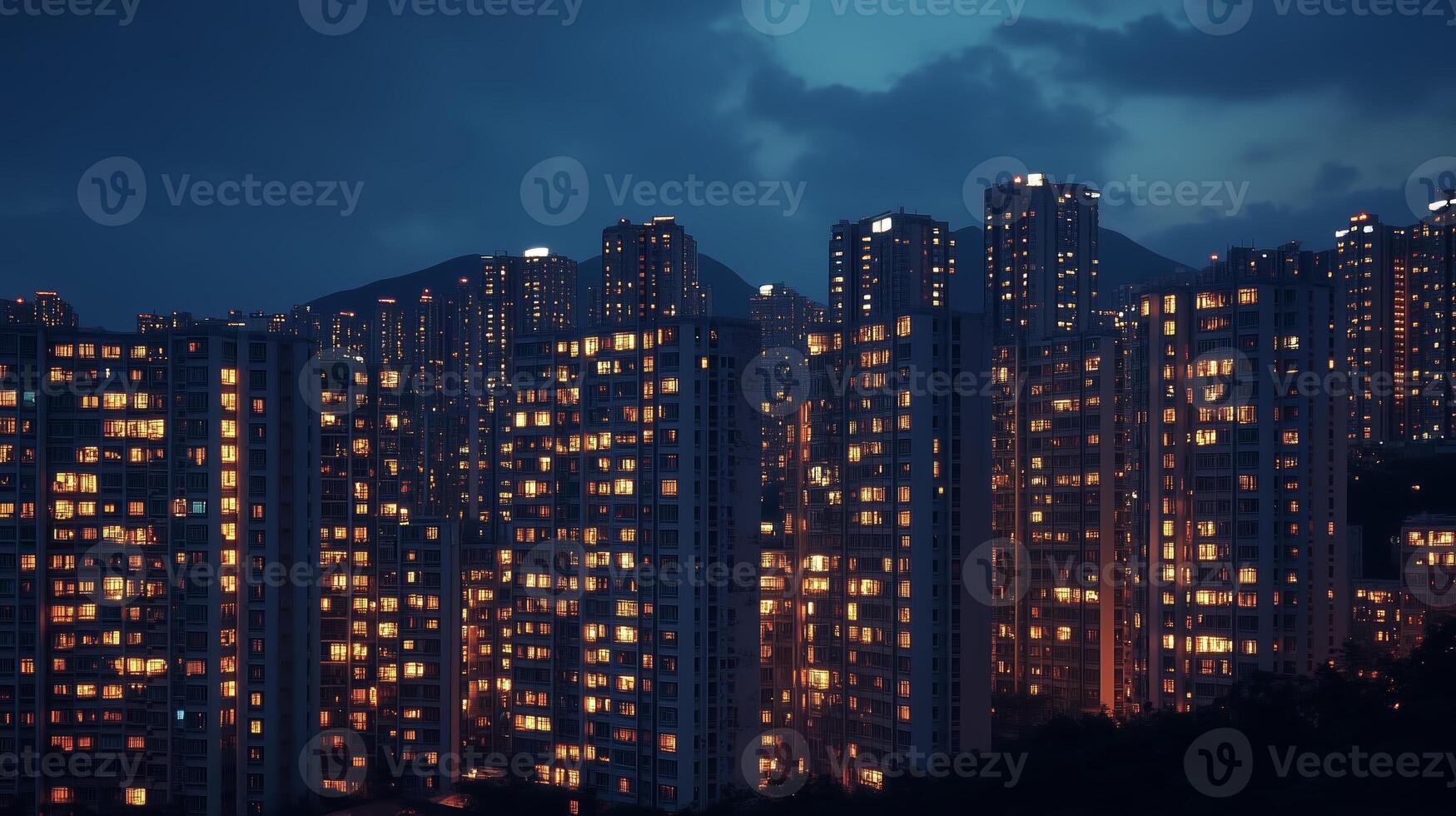 A bustling urban skyline at twilight with illuminated high-rise buildings and a backdrop of distant mountains photo