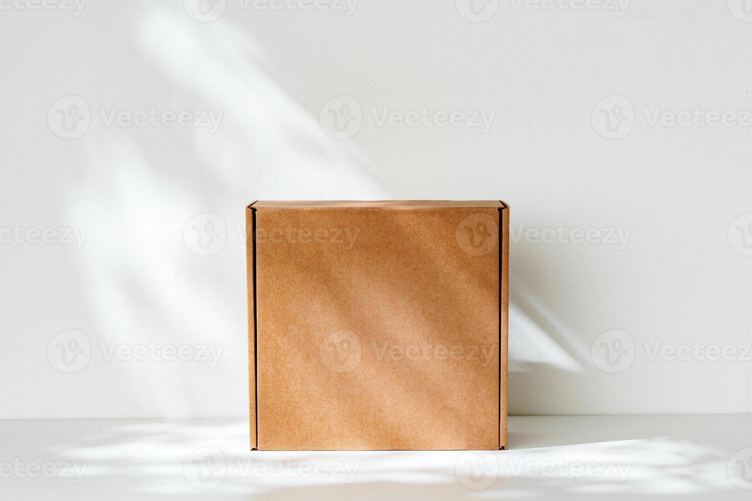 Simple brown cardboard box positioned on a white surface with soft angled shadows in natural light photo