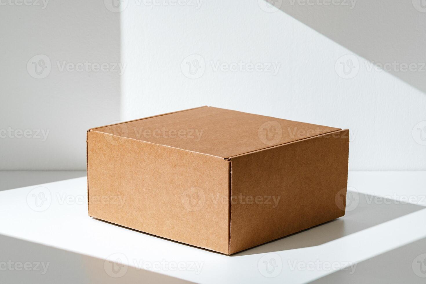 Simple brown cardboard box positioned on a white surface with soft angled shadows in natural light photo