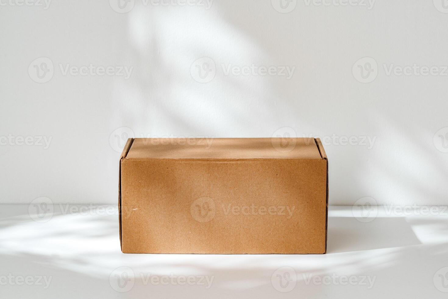 Simple brown cardboard box positioned on a white surface with soft angled shadows in natural light photo