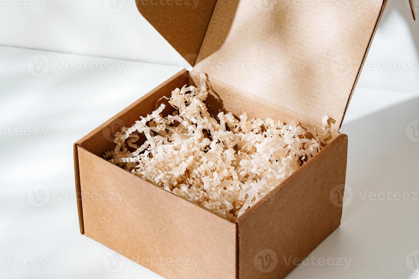 A simple brown gift box with natural filling sits elegantly on a light surface, capturing soft shadows photo