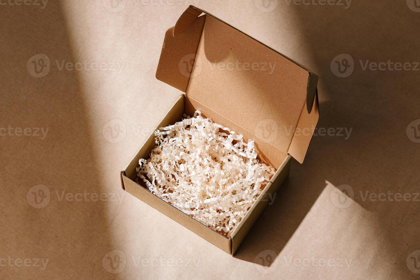Open cardboard box with shredded paper packaging resting on a light brown surface illuminated by soft natural light photo
