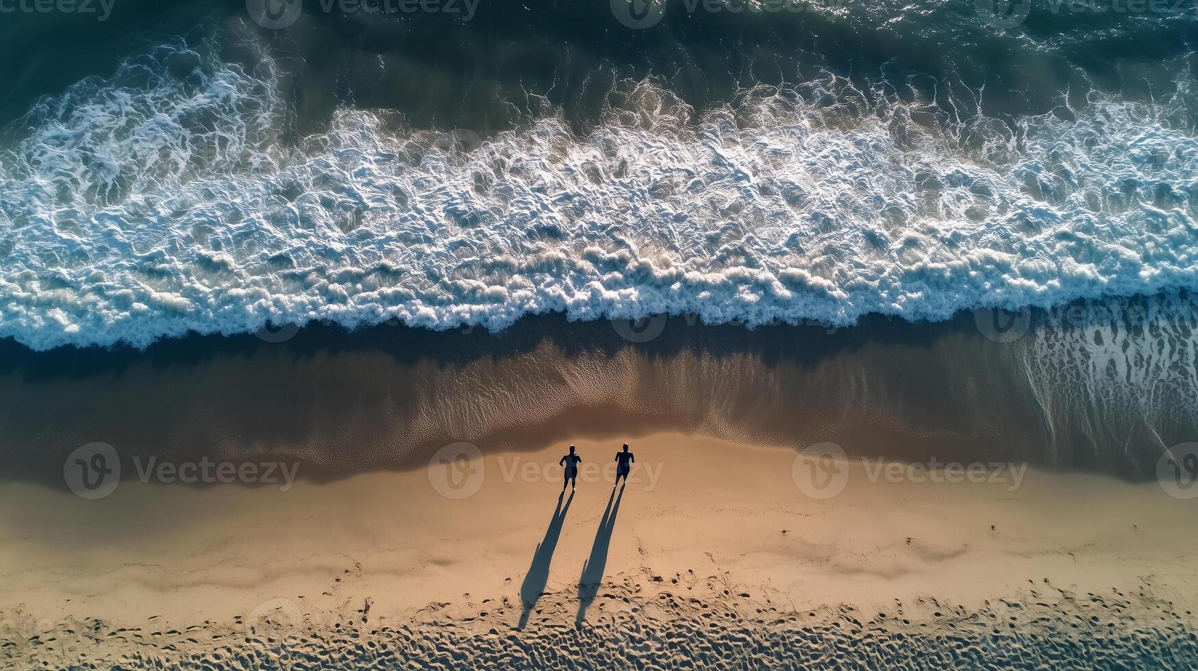 Two figures walking along the shoreline at sunset with waves gently lapping the golden sand beach photo