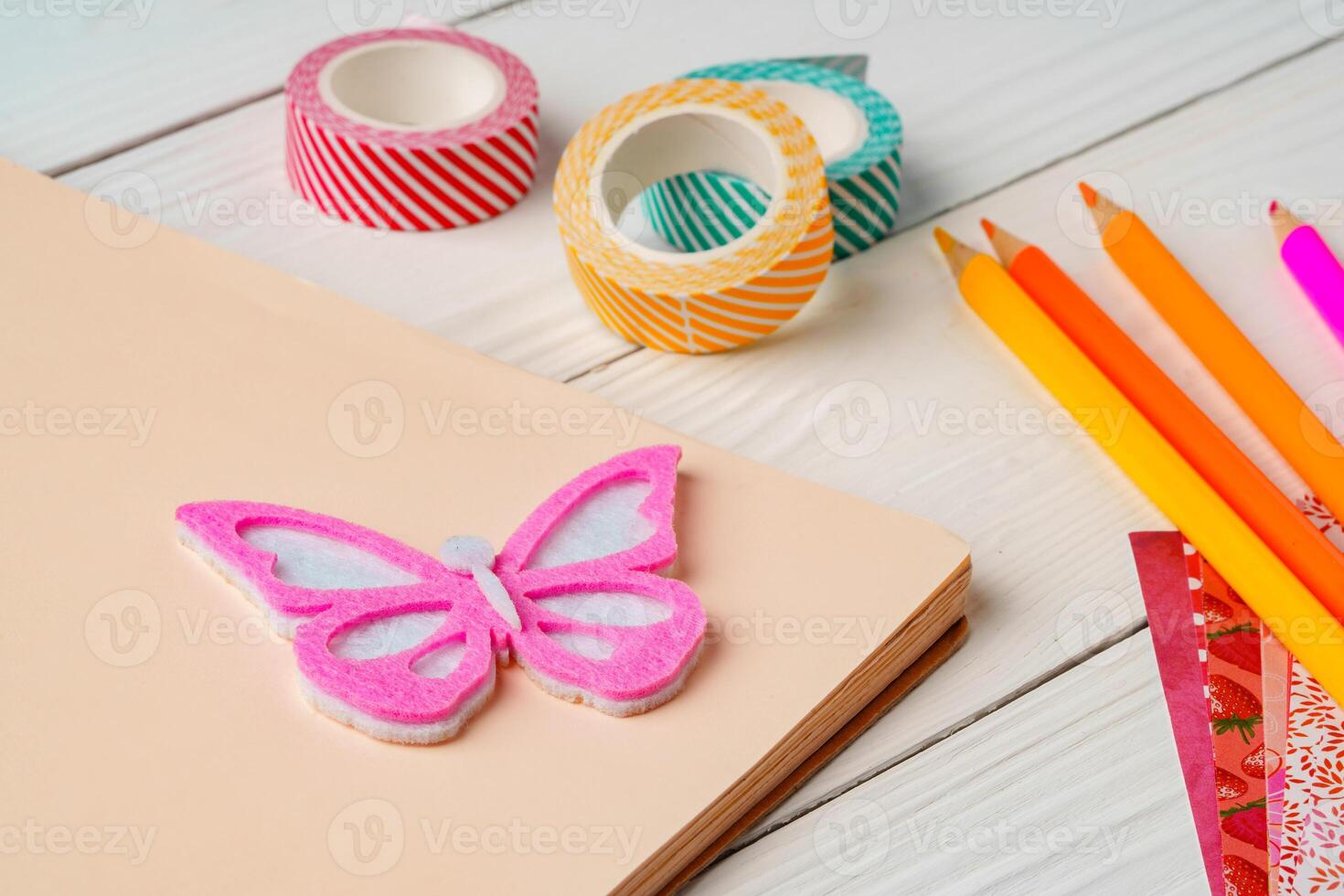 Colorful stationery arrangement with a butterfly sticker on a blank notebook at a wooden table in natural light photo