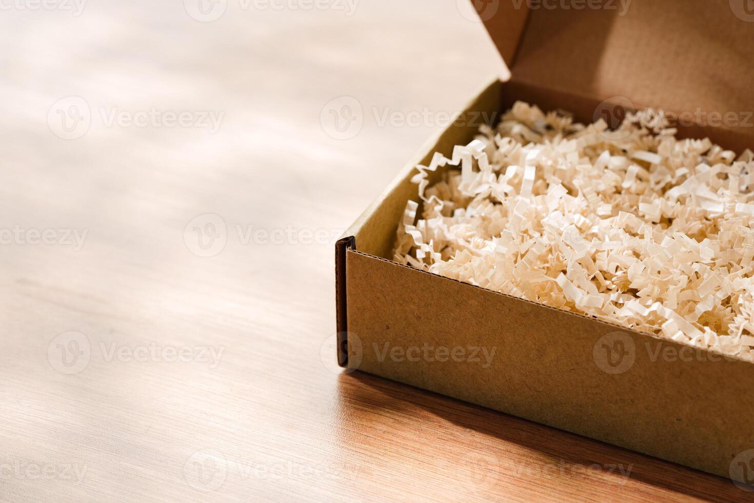 Open cardboard box with shredded paper filling on a wooden table photo