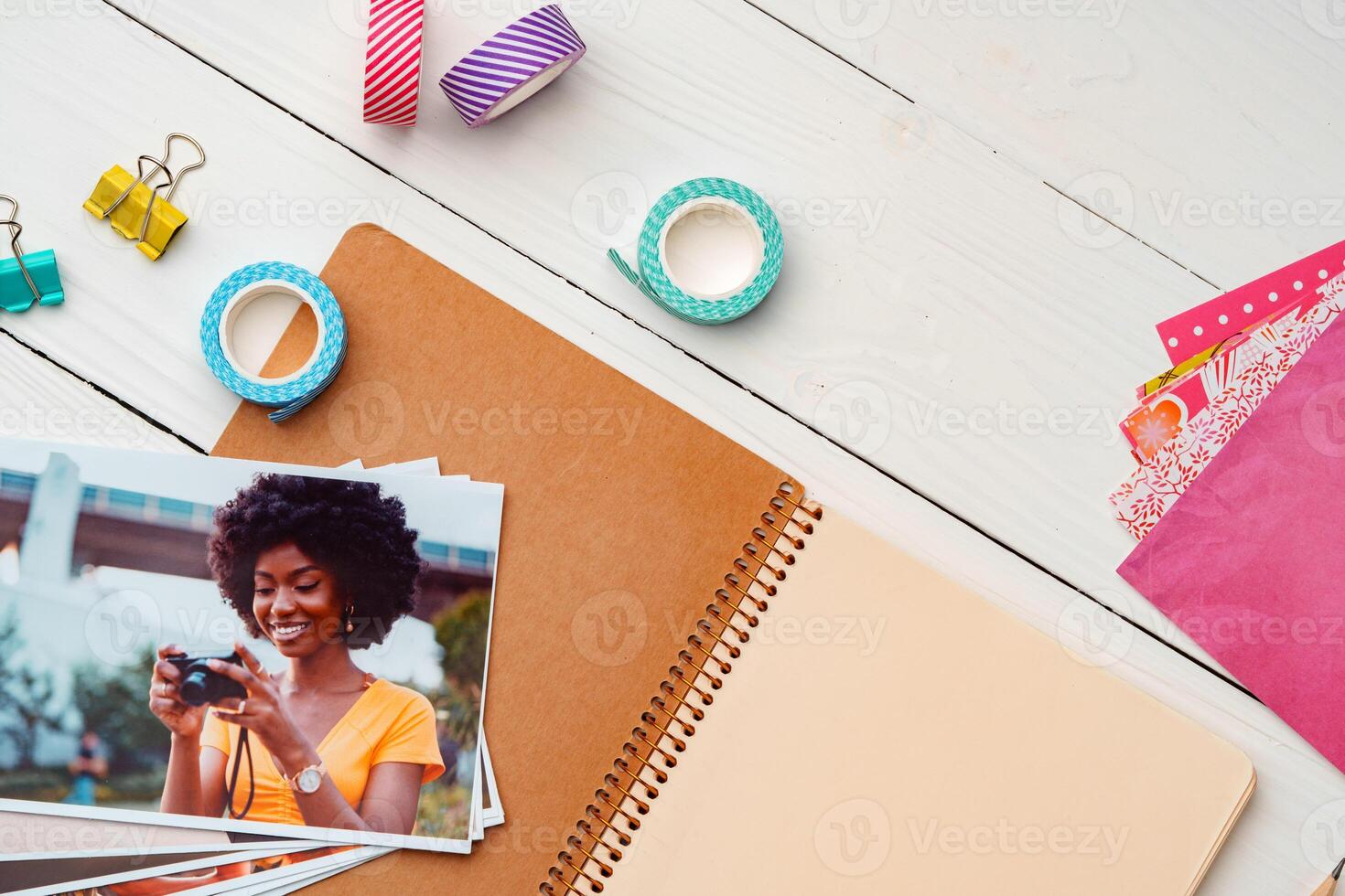 Photo of young woman cwith a camera surrounded by stationery and printed photos on a desk