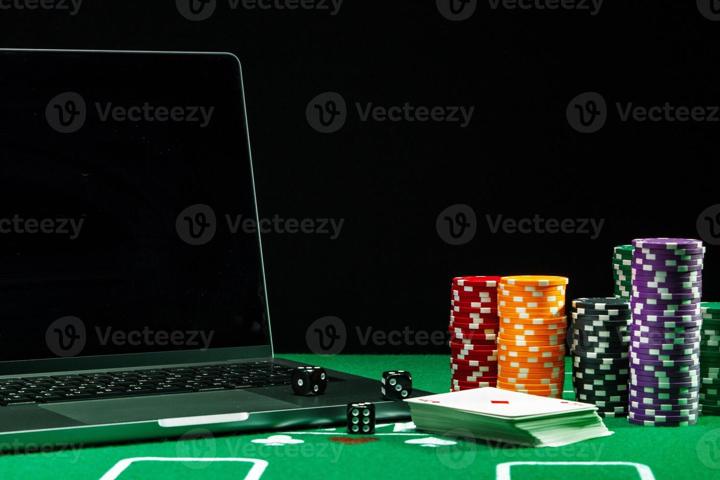 A laptop and poker chips arranged on a green felt table in an indoor gaming setup during a nighttime gambling session photo