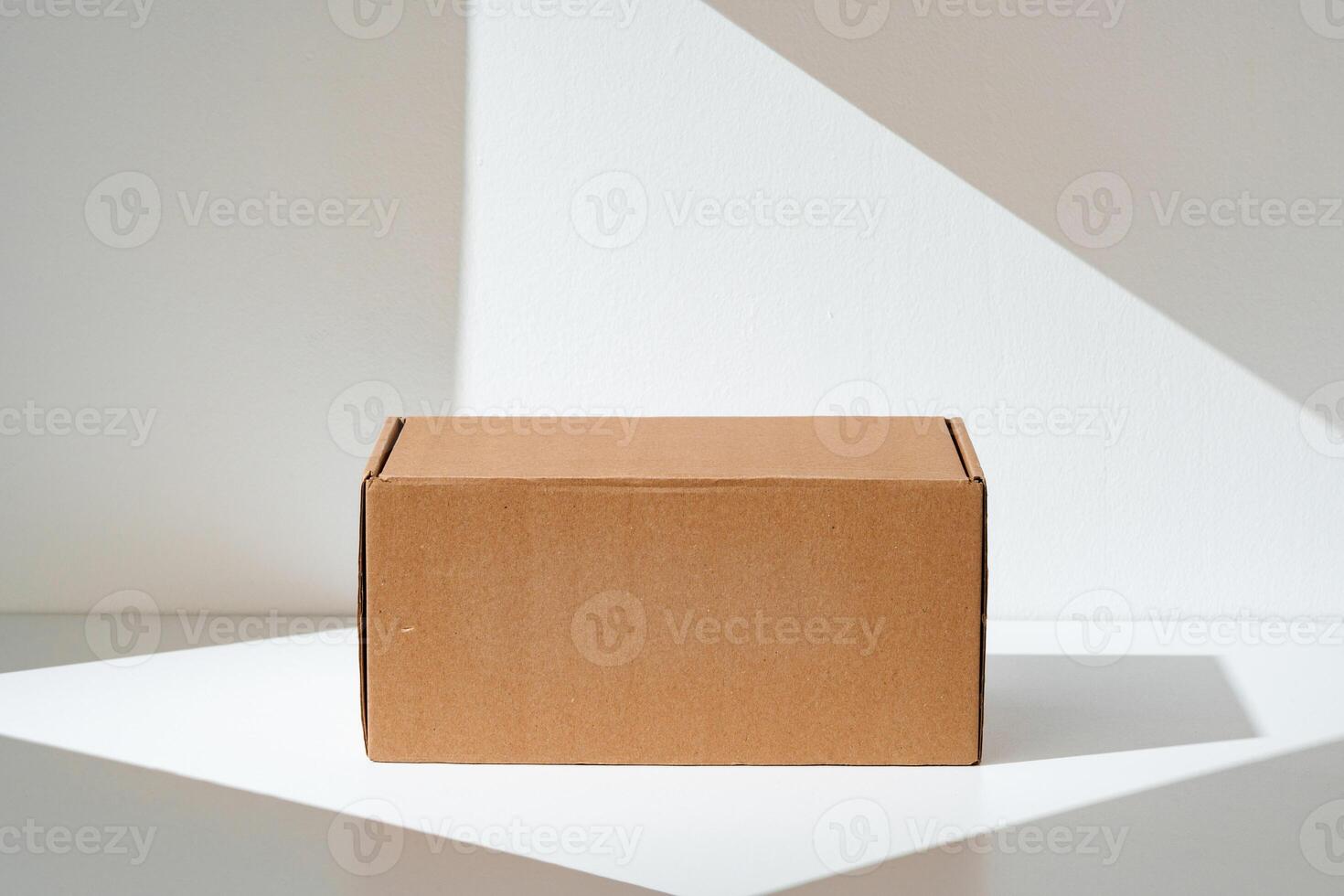 Simple brown cardboard box positioned on a white surface with soft angled shadows in natural light photo