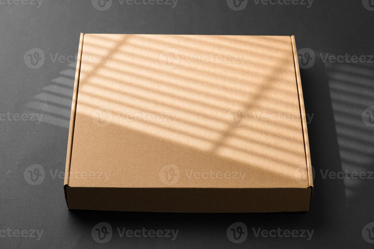 A cardboard box casting shadows on a dark surface in a striped light pattern photo