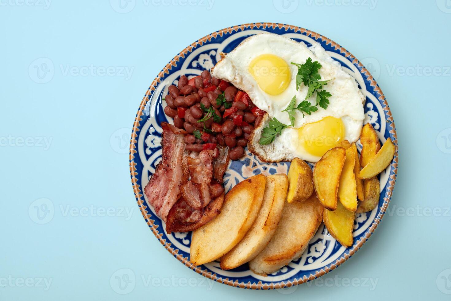 Delicious breakfast plate featuring eggs, beans, bacon, and potato wedges served on a decorative dish photo